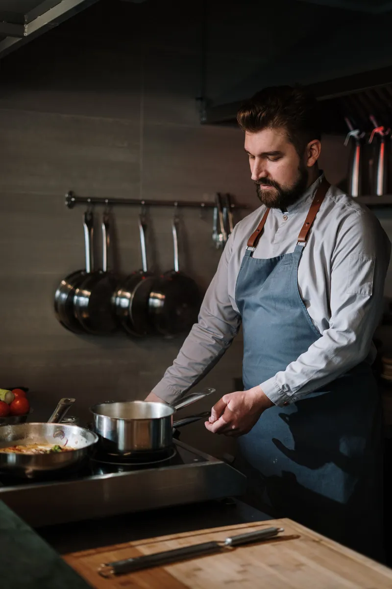 Cocinero profesional usando ollas de acero inoxidable en los fogones